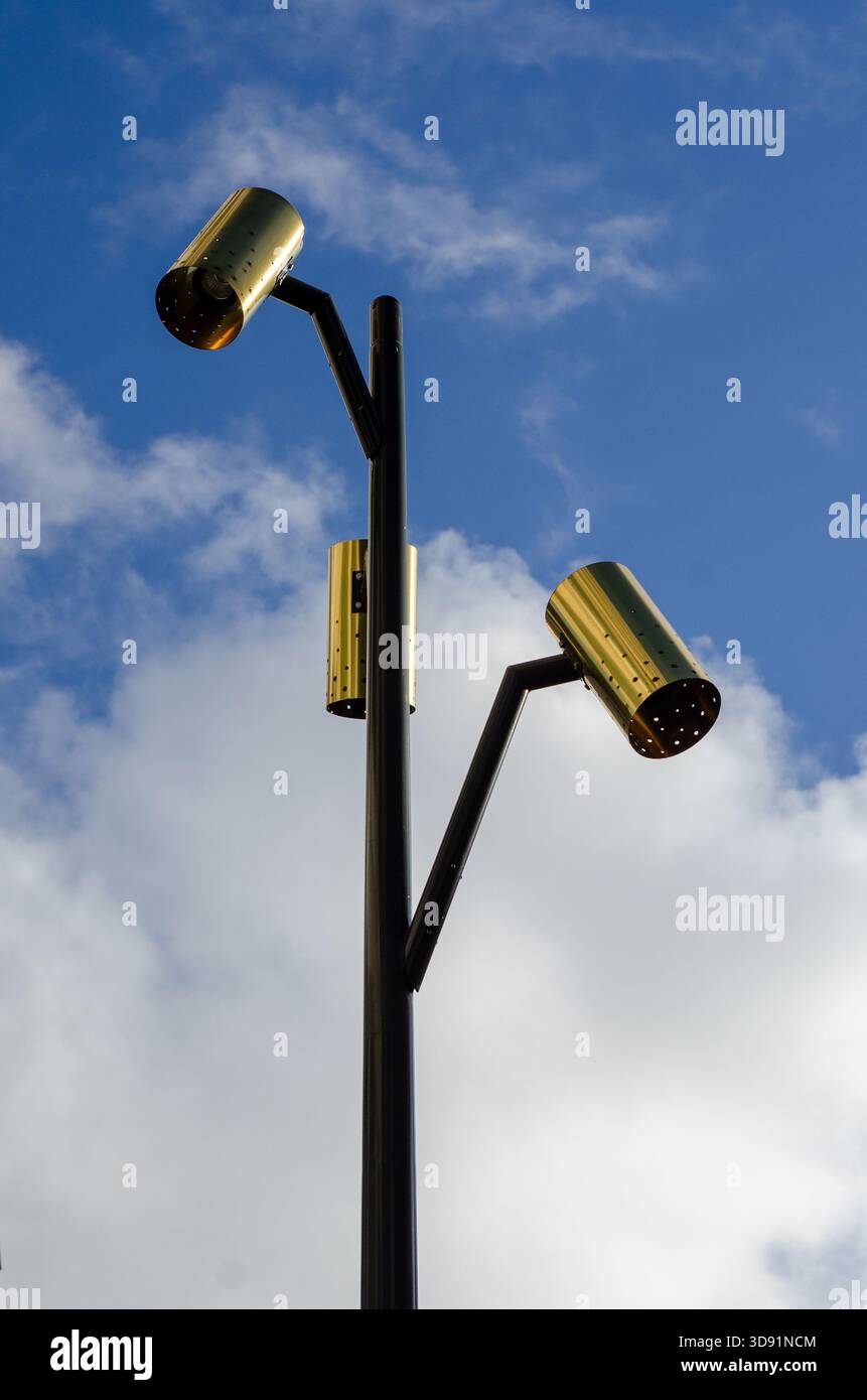 Moderner Schwarzlichtpfosten mit drei verschiedenen goldenen, zylindrischen Lampen vor einem blauen Himmel mit dramatischen weißen Wolken. Stockholm, Schweden. Stockfoto