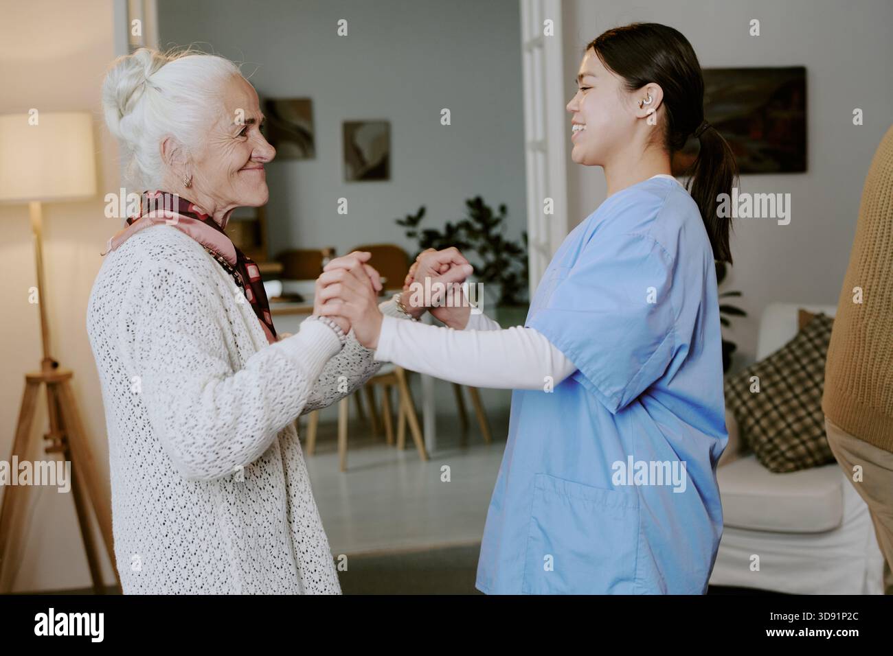 Eine ältere Frau lächelt, während sie die Hände mit der jungen Hispanic Schwester hält Stockfoto