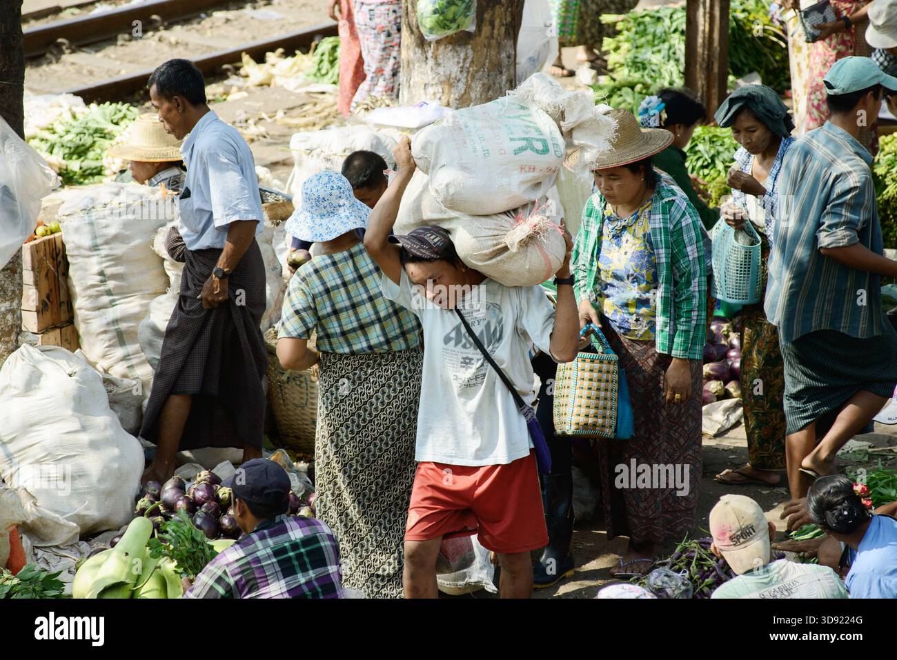 22/2014 – Yangon, Myanmar – Ein Mann trägt einen schweren Sack durch den Bahnhofsmarkt in Yangon, wo die Händler Gemüse und Waren direkt verkaufen Stockfoto