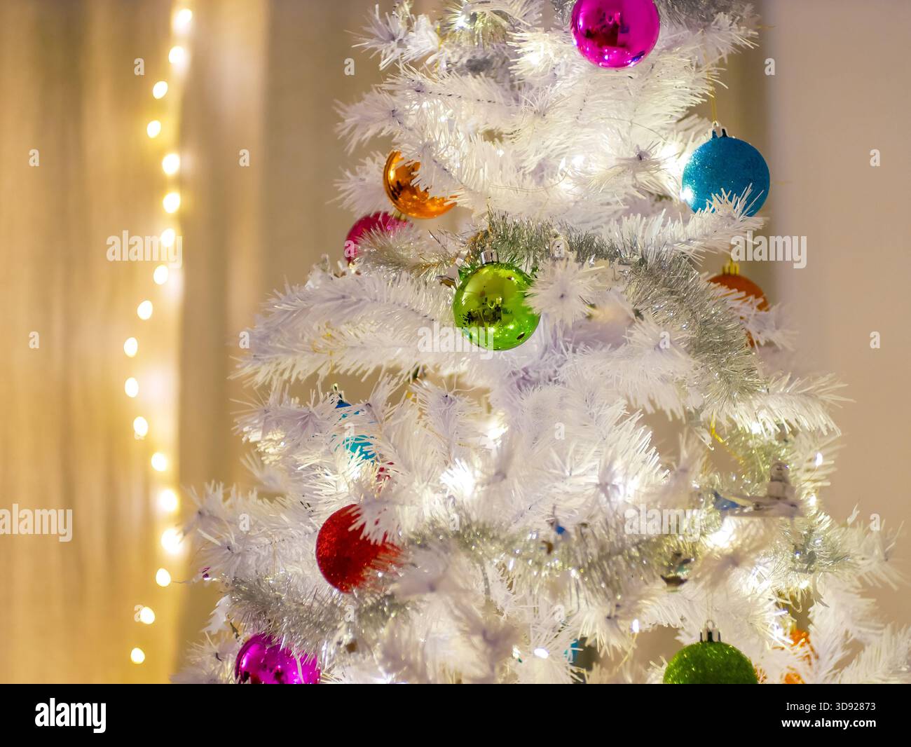 Nahaufnahme eines weißen künstlichen Weihnachtsbaums mit lebendigen Ornamenten und festlichen Lichtern. Feiertags-, Winter- und Feiertagsthemen. Stockfoto