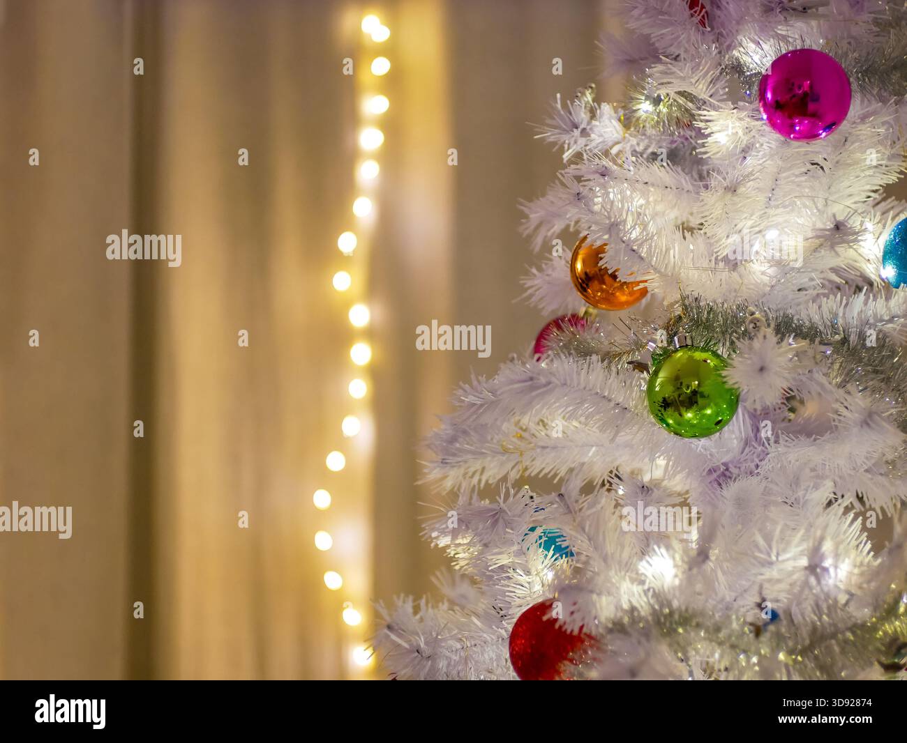 Nahaufnahme eines weißen künstlichen Weihnachtsbaums mit lebendigen Ornamenten und festlichen Lichtern. Feiertags-, Winter- und Feiertagsthemen. Stockfoto
