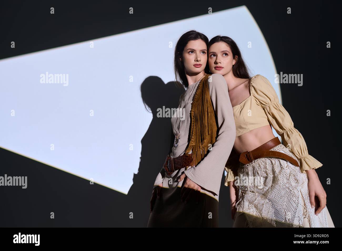 Junge, schöne Zwillingsschwestern zeigen ihre trendigen Outfits in einem kreativen und künstlerischen Umfeld. Stockfoto