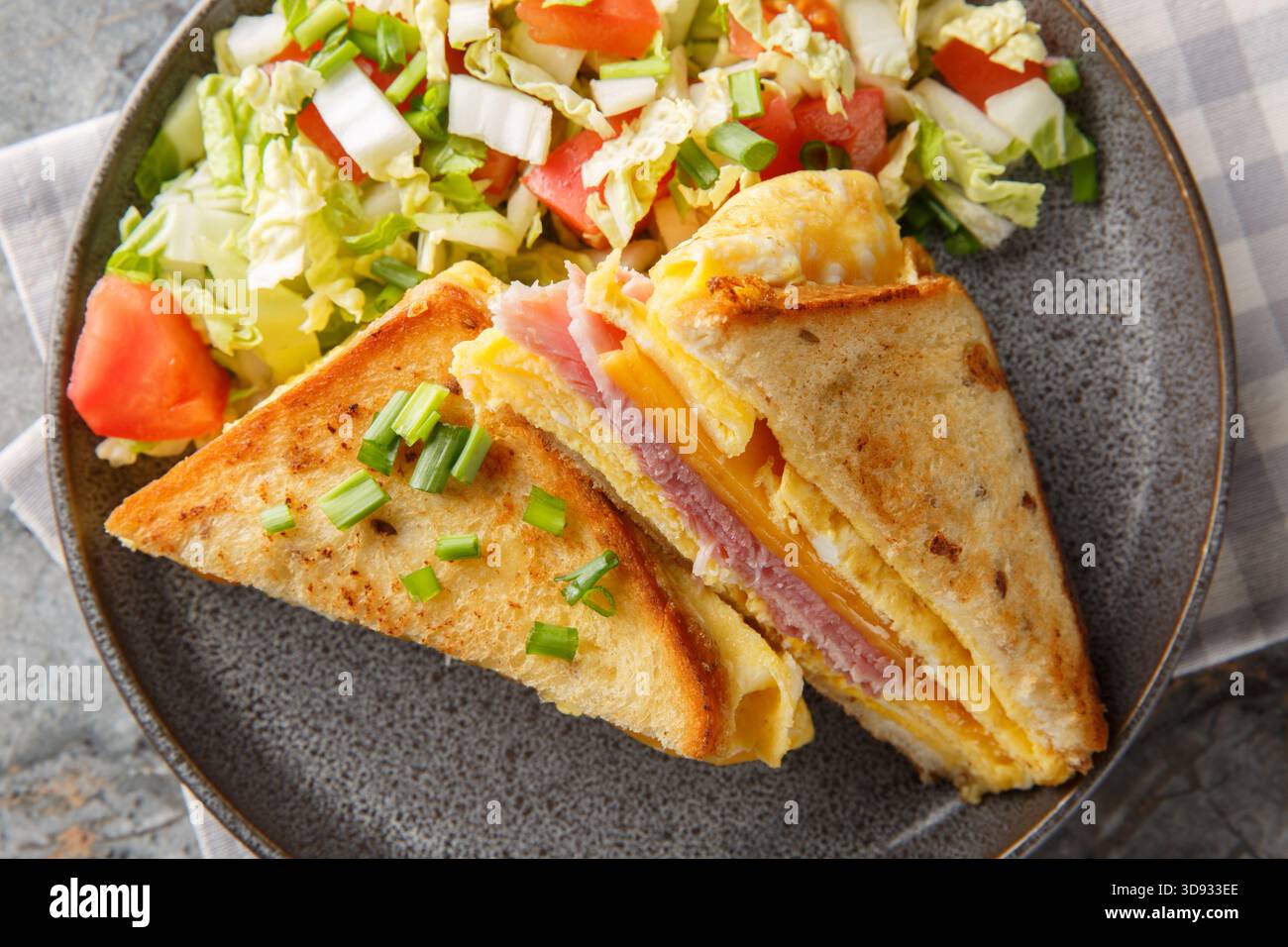 Warmes Sandwich mit Eieromelett, Käse und Schinken in Nahaufnahme auf einem Teller auf dem Tisch. Horizontale Draufsicht von oben Stockfoto