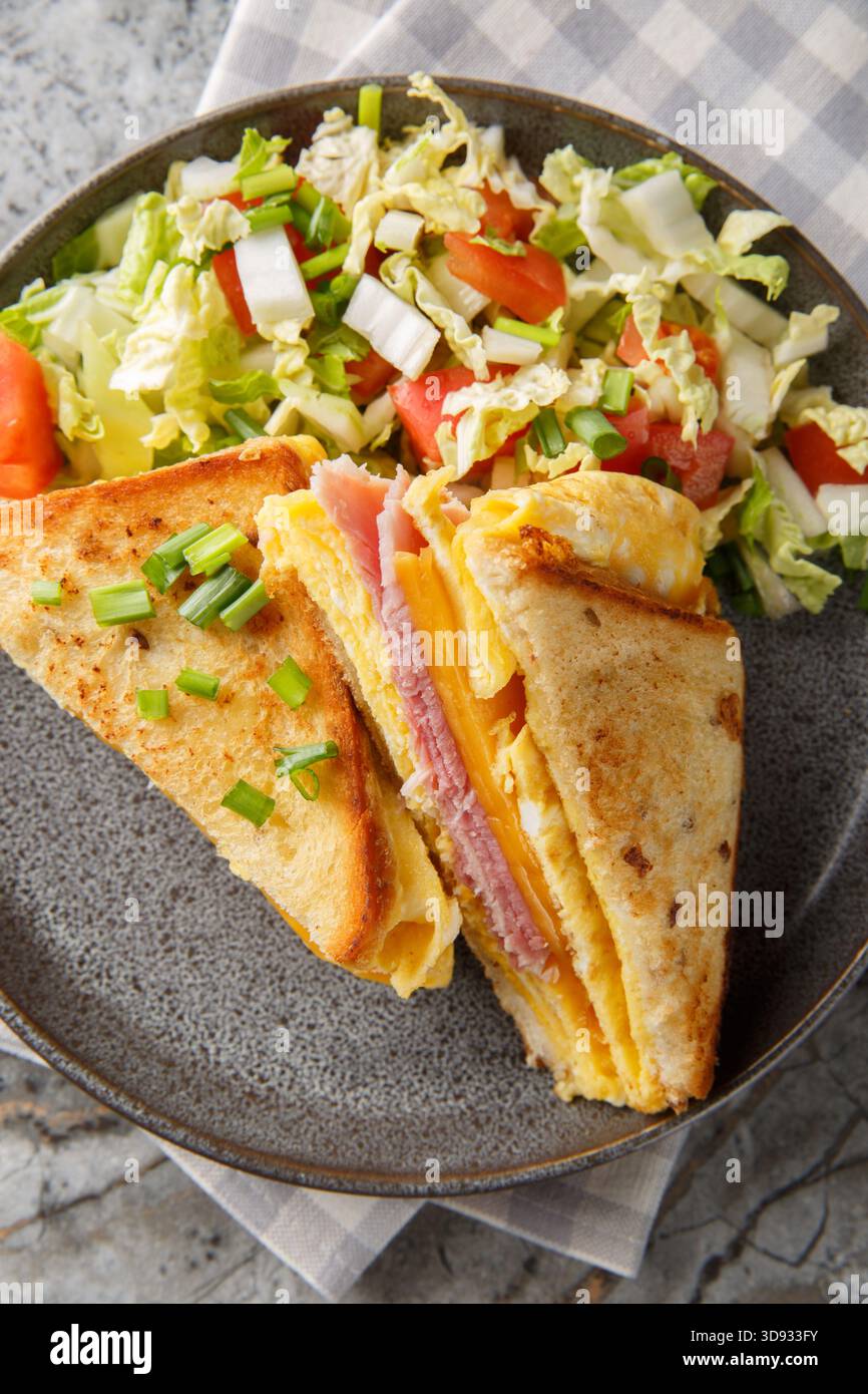 One-Pan Egg Toast mit Schinken und geschmolzenem Käse, serviert mit frischem Salat in der Nähe auf dem Teller auf dem Tisch. Vertikale Draufsicht von oben Stockfoto