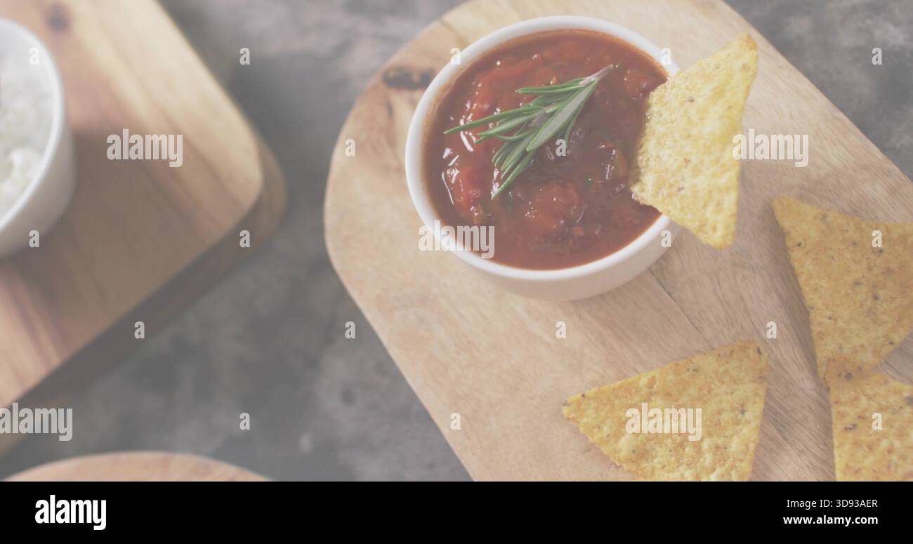 Zeigt eine weiße Schüssel mit groben Tomatensalsa mit Rosmarin auf Holzbrett, dunklem Schiefer, Nachos, Salz Stockfoto
