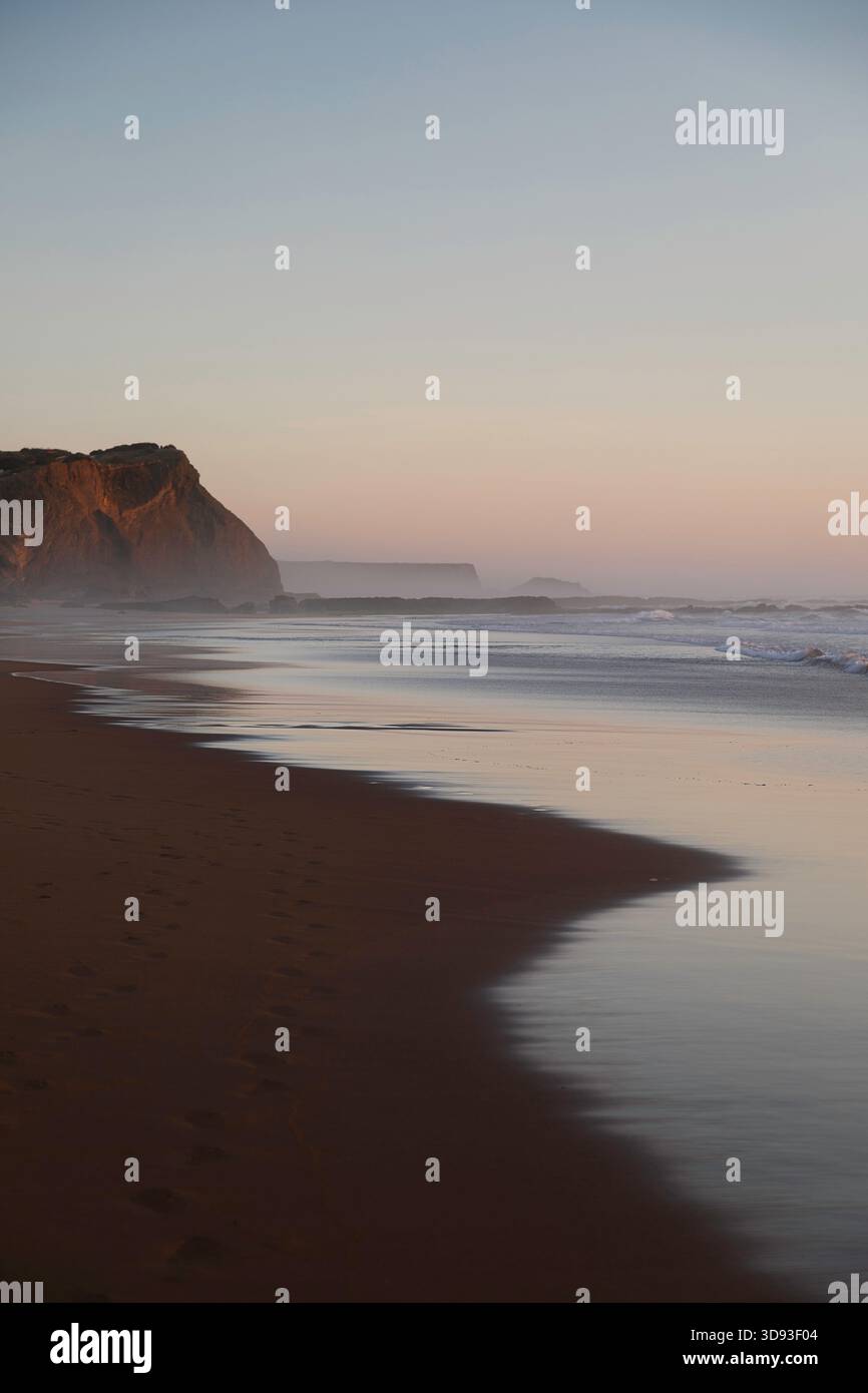 Wasser reflektiert das rosa Licht der untergehenden Sonne am Praia de Monte Clérigo, Algarve Stockfoto