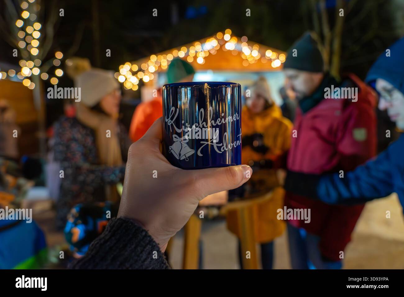11.28.2025 - Bad Kirchheim, Österreich: Hand, die eine Tasse mit einem festlichen Tisch auf einem Wintermarkt mit warmem Licht und Kerzen hält Stockfoto