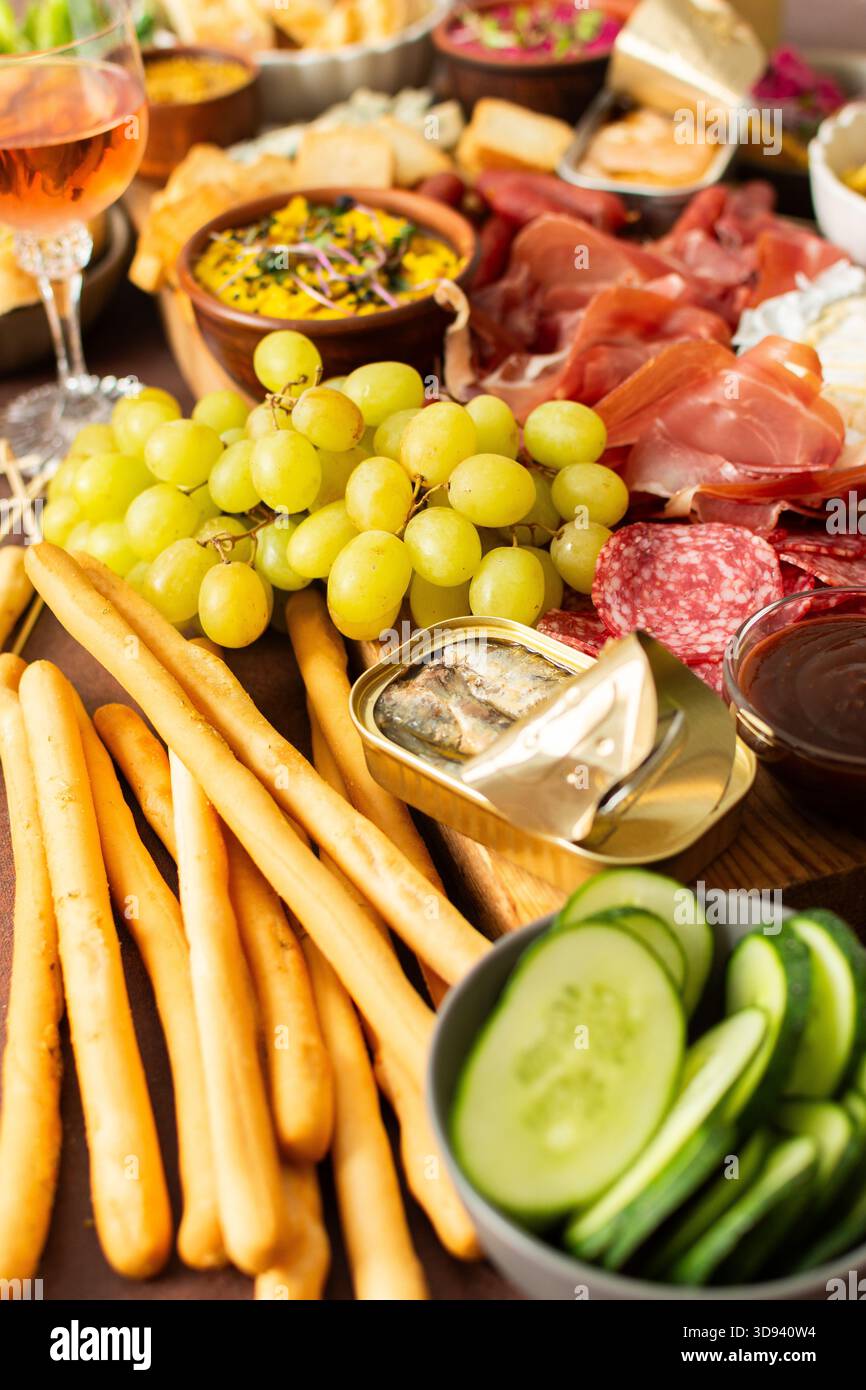 Versammelt um eine wunderschön gestaltete Wurstplatte gefüllt mit verschiedenen Käsesorten, köstlichen Würstchen, cremigem Hummus und frischen Trauben. Perfekt für Stockfoto