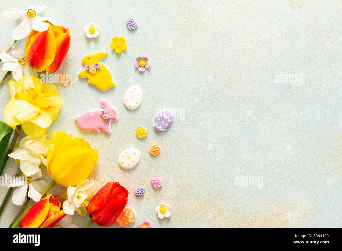 Leuchtende Tulpen und Narzissen umgeben verspielte Osterkekse und Bonbons, die den lebhaften Geist der Frühlingsfeste und Feiertage zum Ausdruck bringen Stockfoto