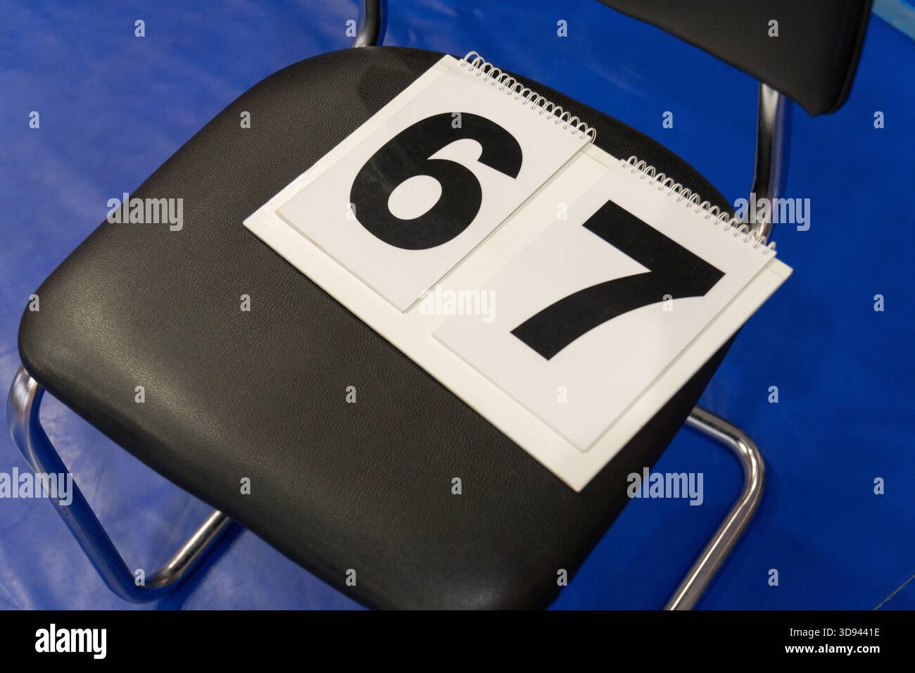 Eine Nahaufnahme von zwei weißen Nummernschildern mit den schwarzen Ziffern 6 und 7, die auf einem schwarzen Polsterstuhl mit verchromten Beinen auf einem liegen Stockfoto