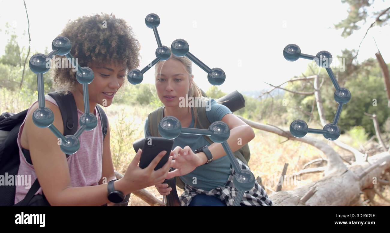 Zwei Wanderer sitzen, Rucksäcke tragen, sich hineinlehnen, Smartphone auf Baumstamm studieren, mit molekularen Modellen Stockfoto