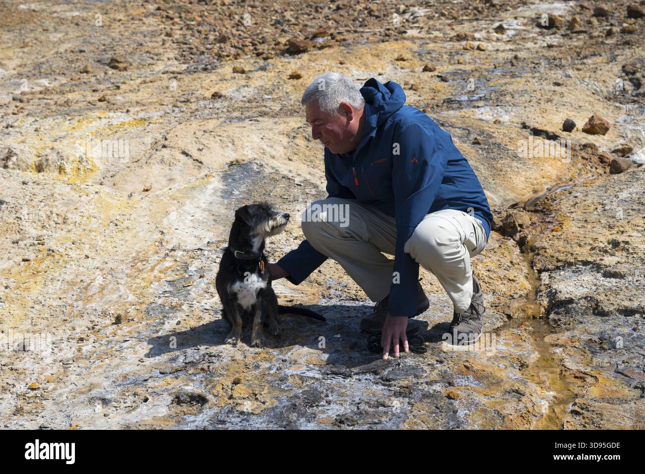 Mann, der mit Hund in einer felsigen, natürlichen Umgebung spielt, in Outdoor-Kleidung gekleidet, Hund und Mann schauen sich gegenseitig an Stockfoto