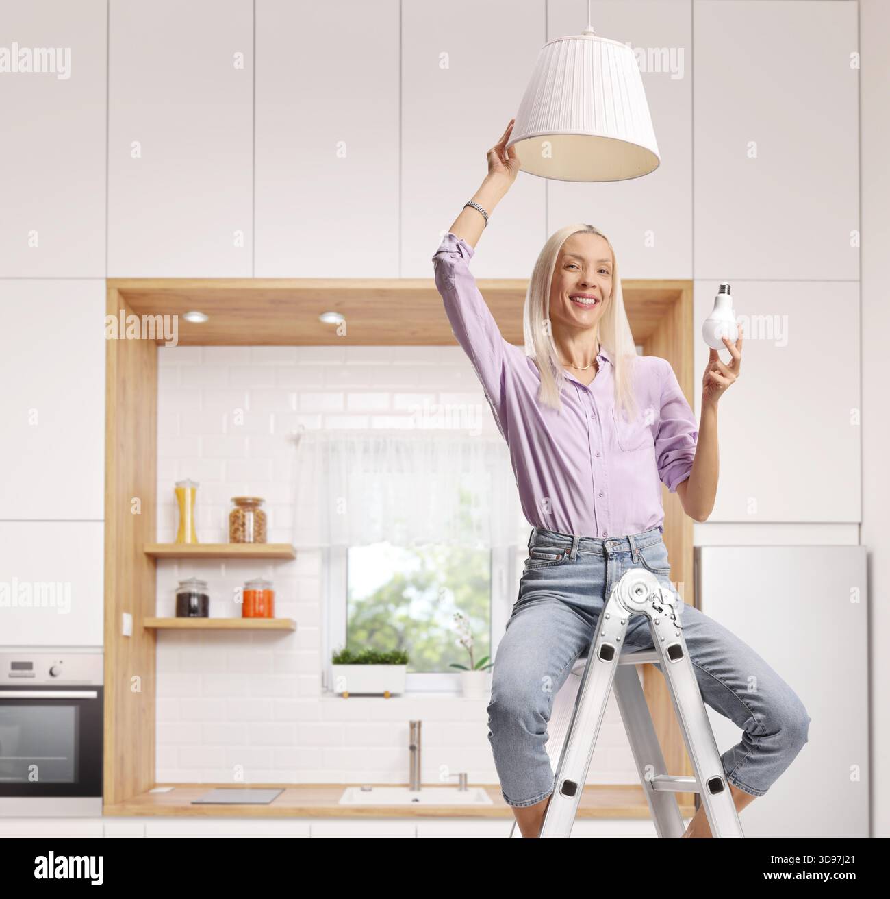 Frau auf einer Leiter, die zu Hause eine Glühbirne in eine Pendelleuchte steckt Stockfoto