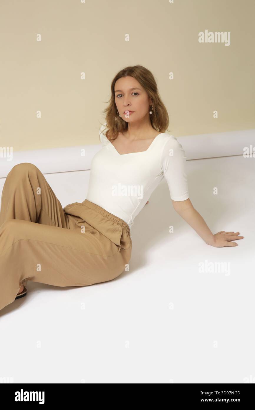 Weibliches Modell mit weißem Hemd und goldener, beigefarbener Hose. Klassische und zeitlose Mode-Kollektion für den Frühling und Sommer. Studio-Aufnahme. Stockfoto