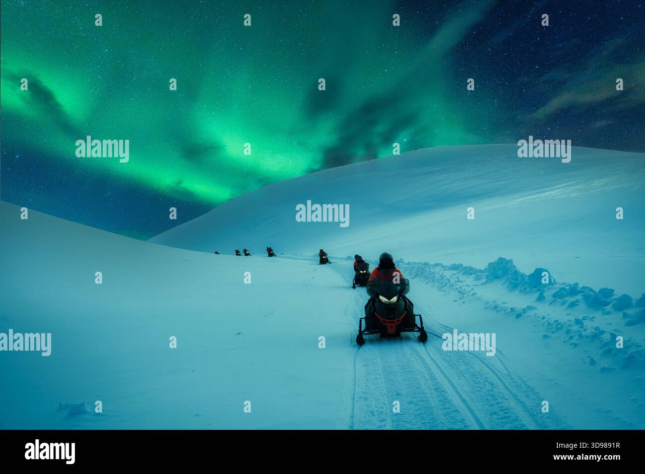 Gruppe von Touristen, die mit dem Schneemobil durch den schneebedeckten Berggletscher mit Nordlichtern am Himmel im Winter auf Island fahren Stockfoto