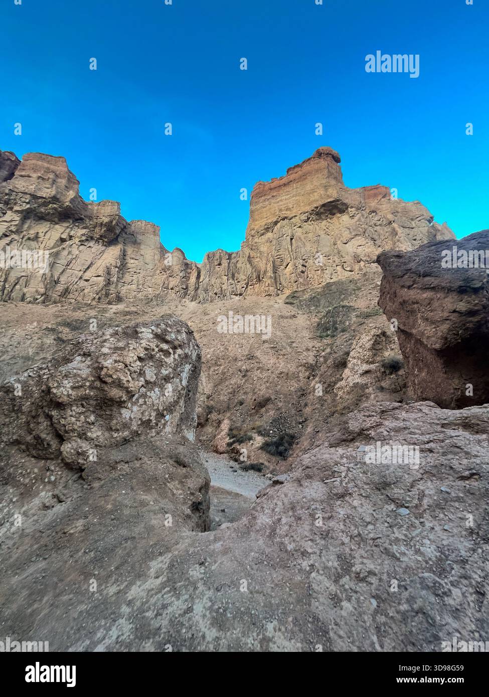 Flacher Blick auf die Felsformationen des Charyn Canyon: Zerklüftete Steinstruktur und burgenähnliche Gipfel vor blauem Himmel. Stockfoto