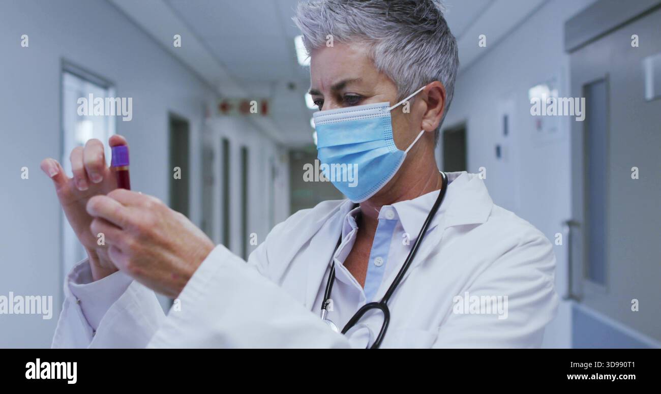 Arzt, der die violette Röhre im Klinikkorridor inspiziert, Stethoskop mit blauer Maske Stockfoto