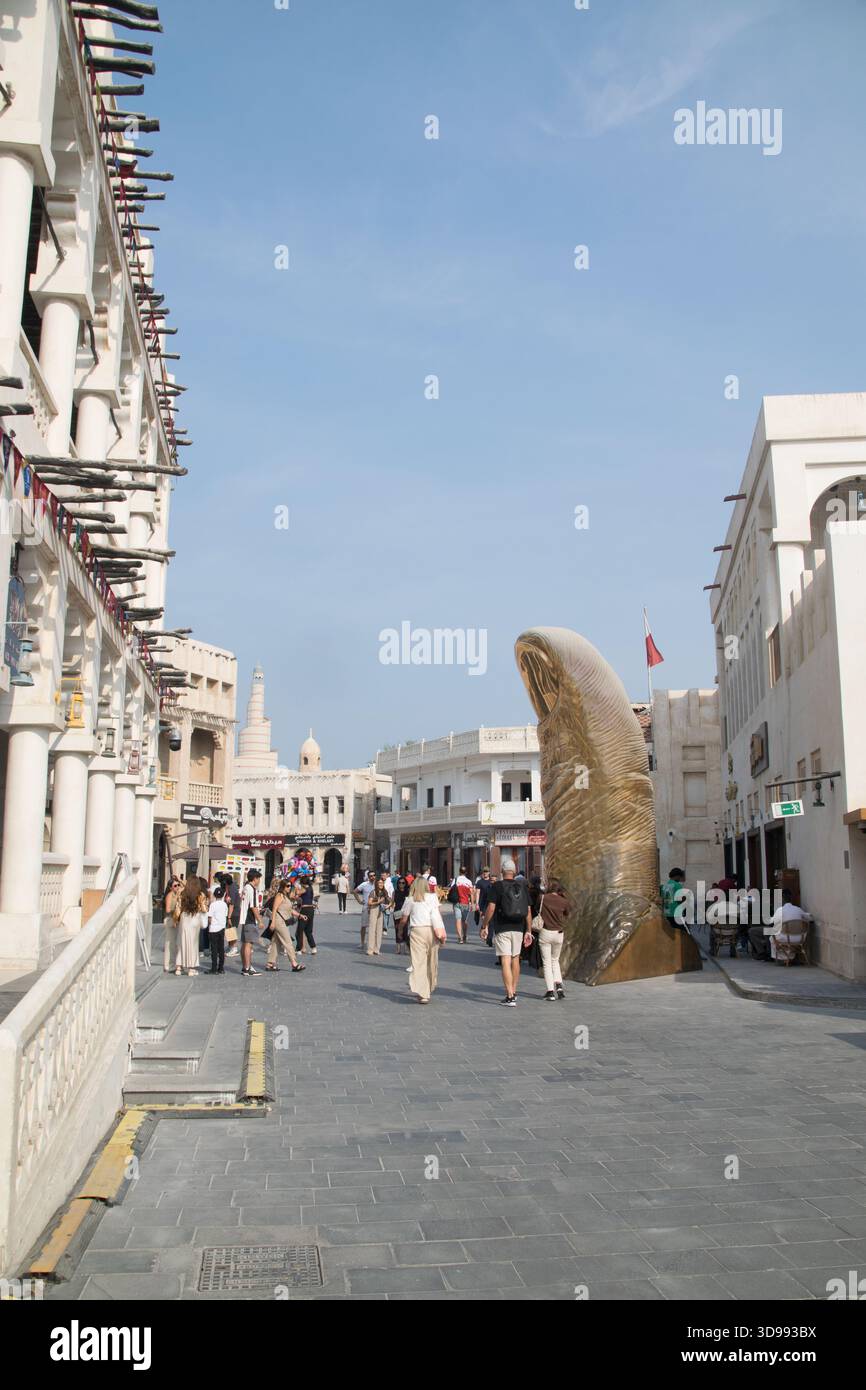 Menschenmassen erkunden den geschäftigen Souq Waqif in Doha, umgeben von einzigartiger Architektur und kulturellen Darbietungen an einem sonnigen Tag. Stockfoto