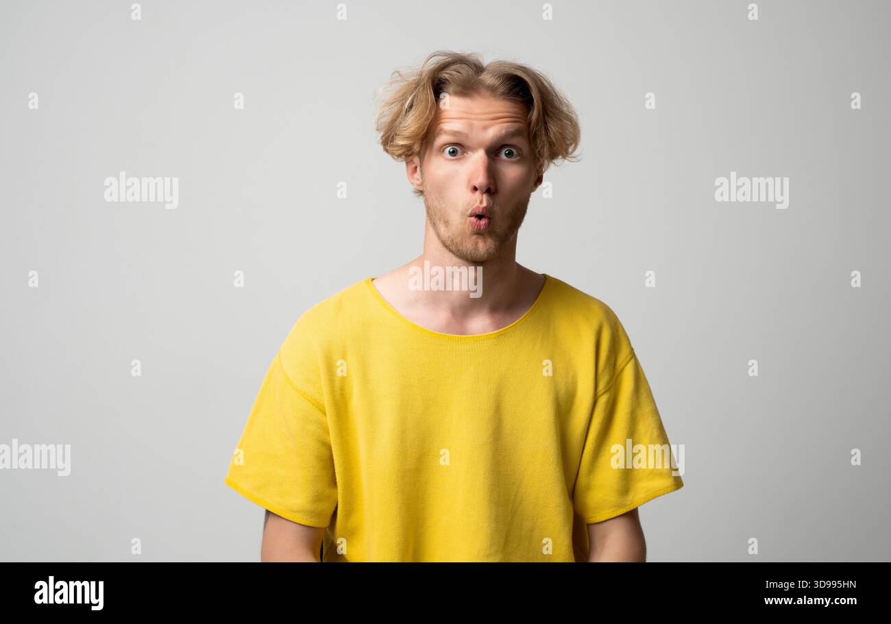 Überraschter junger Mann mit abgerundetem Lippenausdruck und einem klaren neutralen Studio-Porträt nach vorne blickt Stockfoto