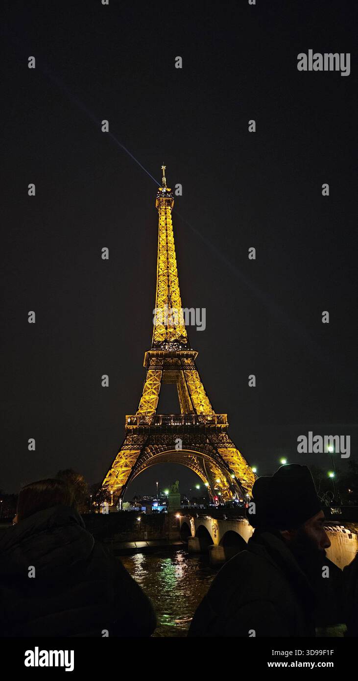 Der Eiffelturm leuchtet nachts in Paris, Frankreich, mit Reflexionen auf nassem Gehweg und lebhafter Menschenmenge. Stockfoto