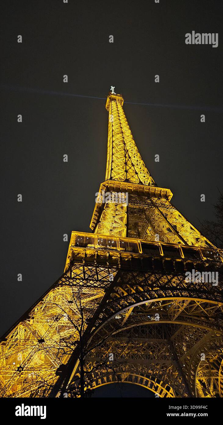 Eiffelturm beleuchtet bei Nacht in Paris, Frankreich, mit goldenen Lichtern und dramatischer, niedriger Sicht. - Smartphone-aufgenommenes Stockfoto