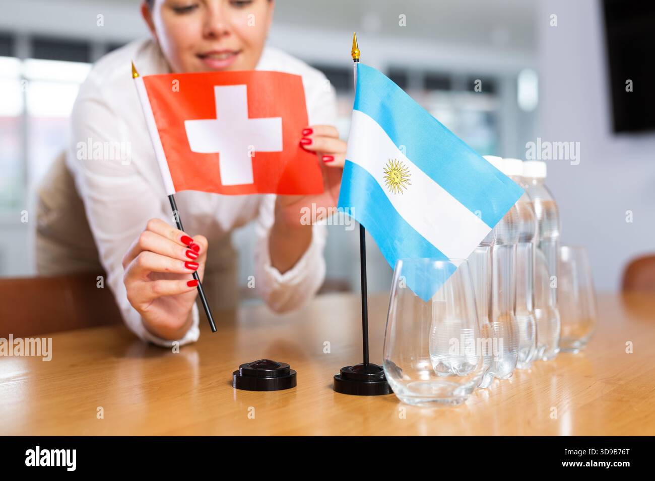 Vorbereitung der Geschäftspräsentation - Sekretärin platziert Flaggen aus Argentinien und der Schweiz auf den Verhandlungstisch Stockfoto