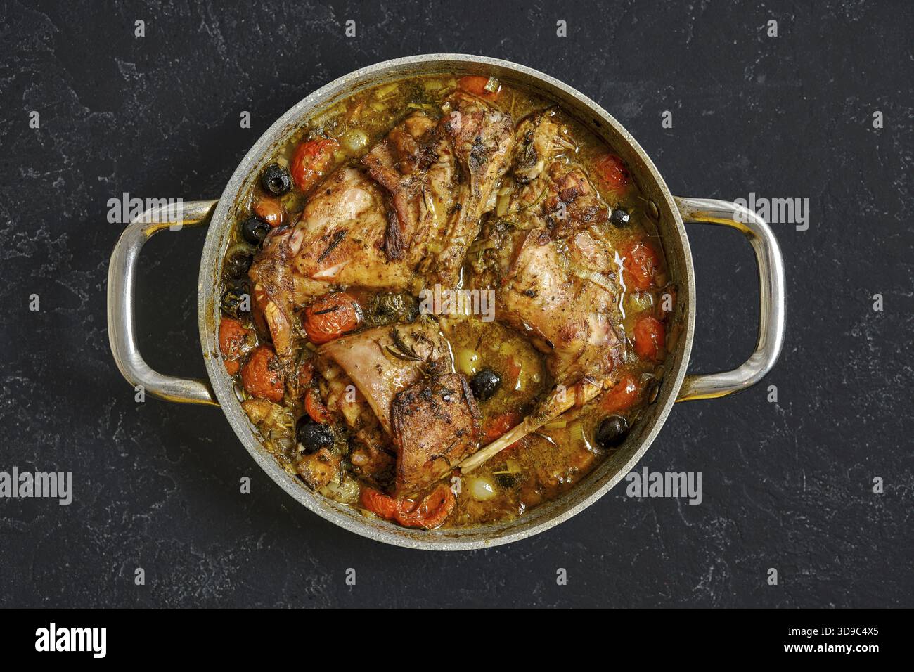 Ein köstlicher Eintopf aus Kaninchen-Hinterschenkel kocht in einem großen Topf, mit saftigem Fleisch, umgeben von Karotten, Oliven und anderem Gemüse in einer reichhaltigen Sauce. Ide Stockfoto