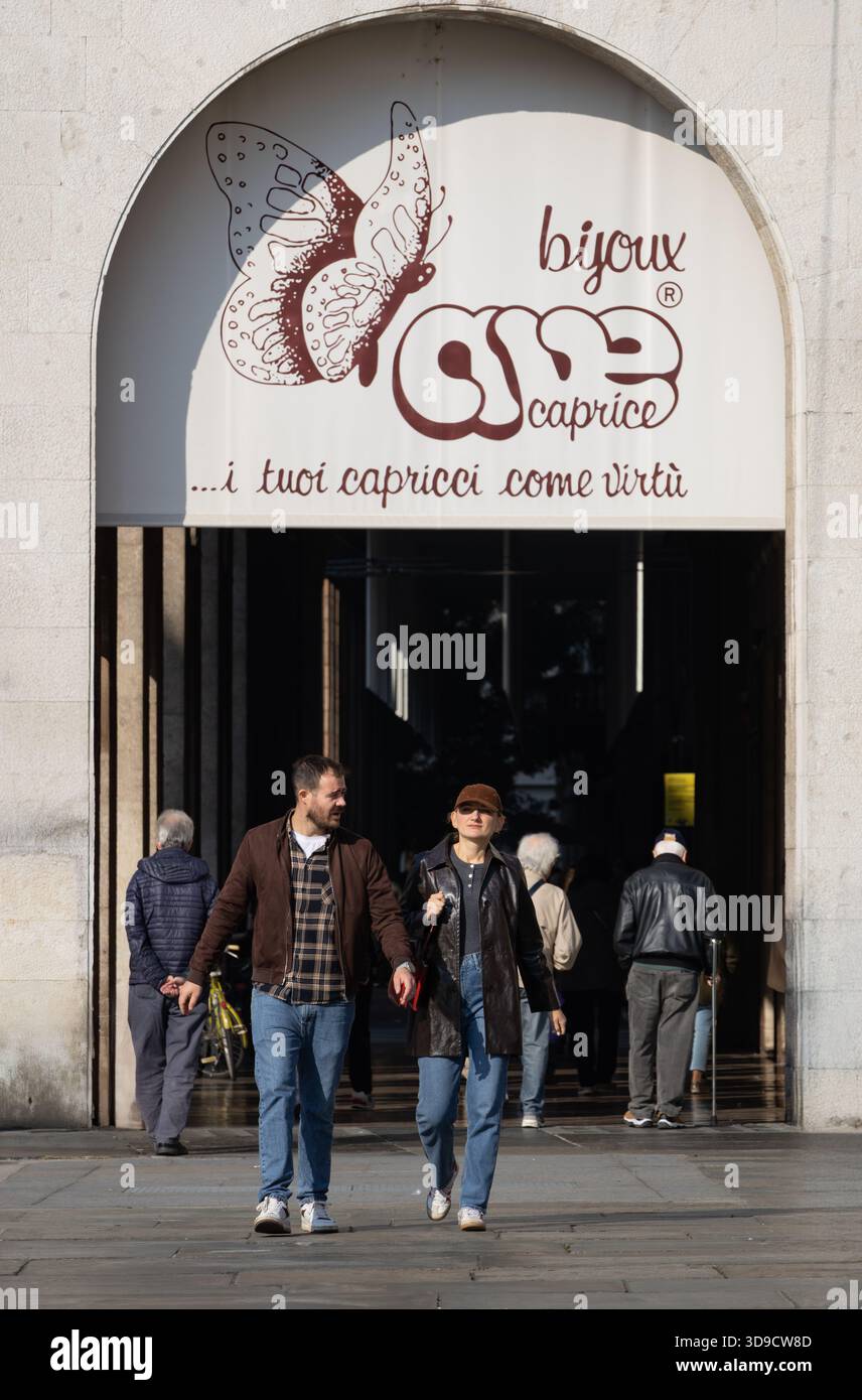 Ein paar Spaziergänge unter einem italienischen Ladenschild mit Schmetterlingslogo und genießen Sonnenlicht und entspannte Atmosphäre im Stadtzentrum. Stockfoto