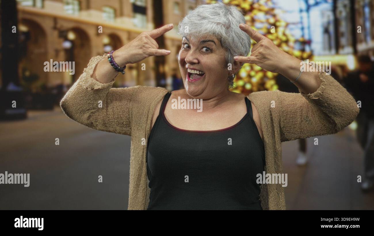 Frau Senior mit Tanktop und Strickjacke, die Steinhandgeste mit Händen und Lächeln im Bauen zeigt; spielerisches Selbstvertrauen. Stockfoto