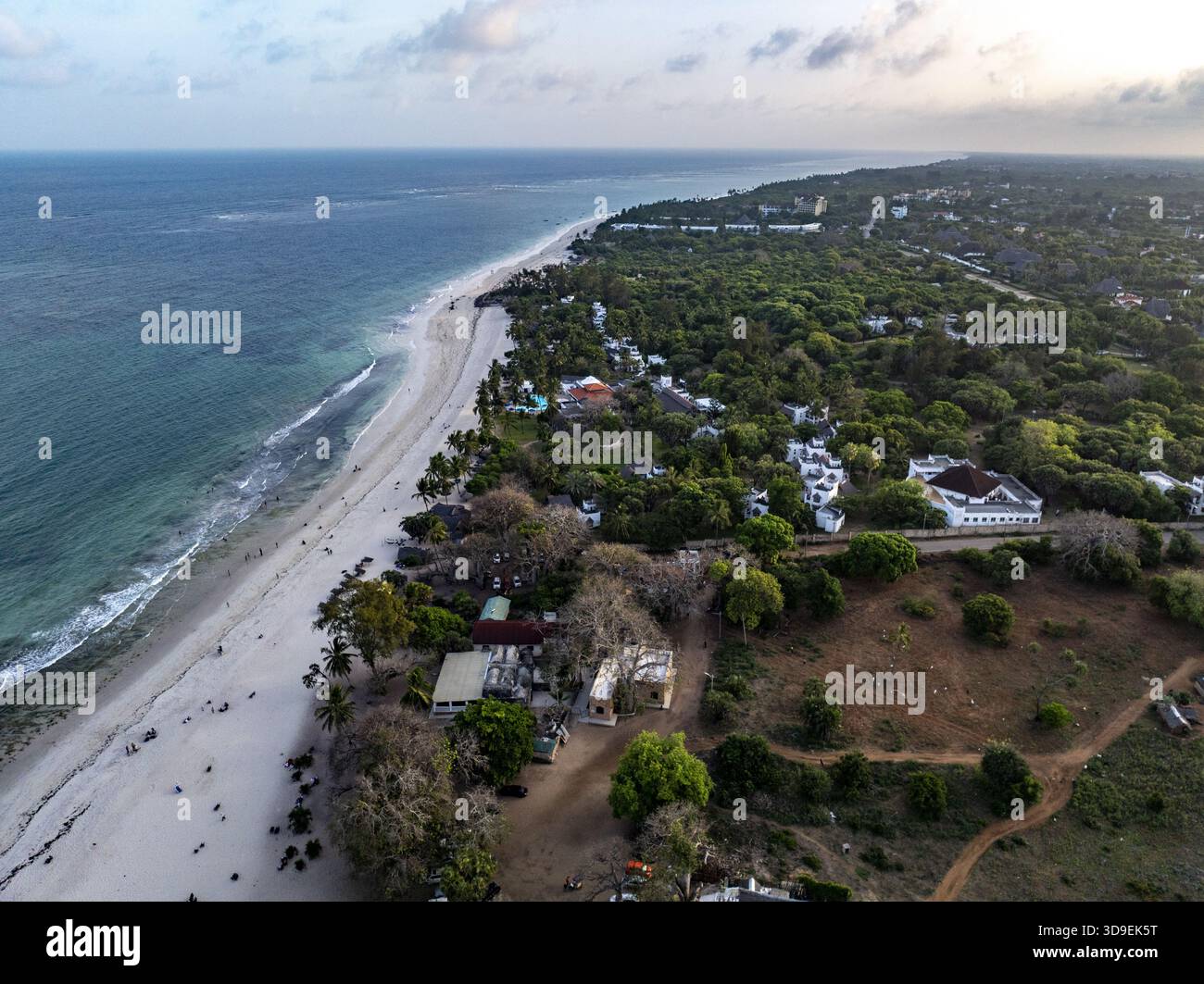 Aus der Vogelperspektive auf das ruhige türkisfarbene Wasser trifft auf die Sandküste, gesäumt von grünen Bäumen und Gebäuden entlang der Küste, Diani, Kwale County, Ke Stockfoto