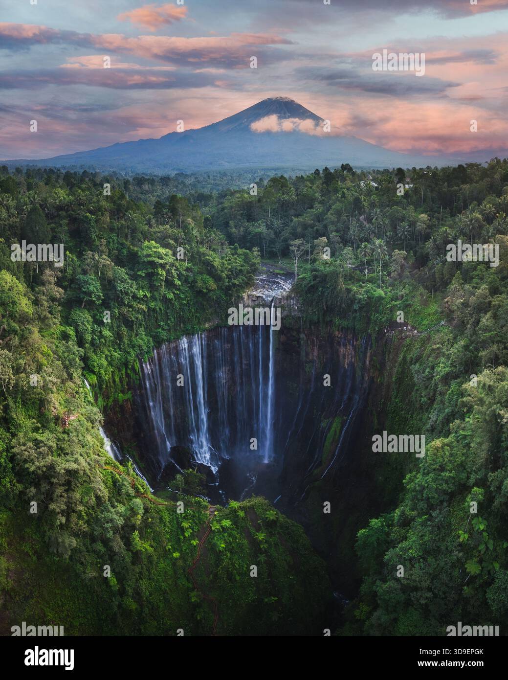 Aus der Vogelperspektive auf den majestätischen Tumpak Sewu Wasserfall, der durch den grünen Dschungel stürzt, mit dem Semeru Berg, umgeben von ätherischen Wolken, Jalan Raya Dampi Stockfoto