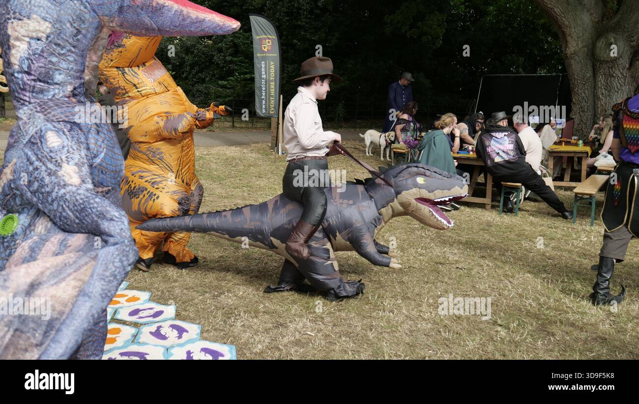 Fantasy Forest Festival 2025 Kostüm Indianer Jones wird von Jurassic Park Inflatable Dinosaurs United Kingdom 2025 verfolgt Stockfoto