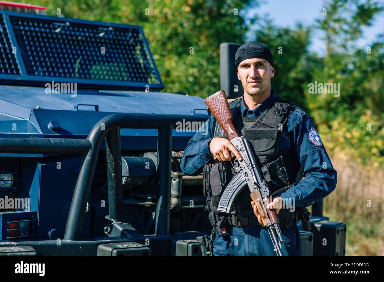 Ein kosovarischer Polizist steht mit einem automatischen Gewehr neben einem gepanzerten Fahrzeug im Grenzgebiet Banjska während erhöhter Sicherheitsmaßnahmen Wache Stockfoto