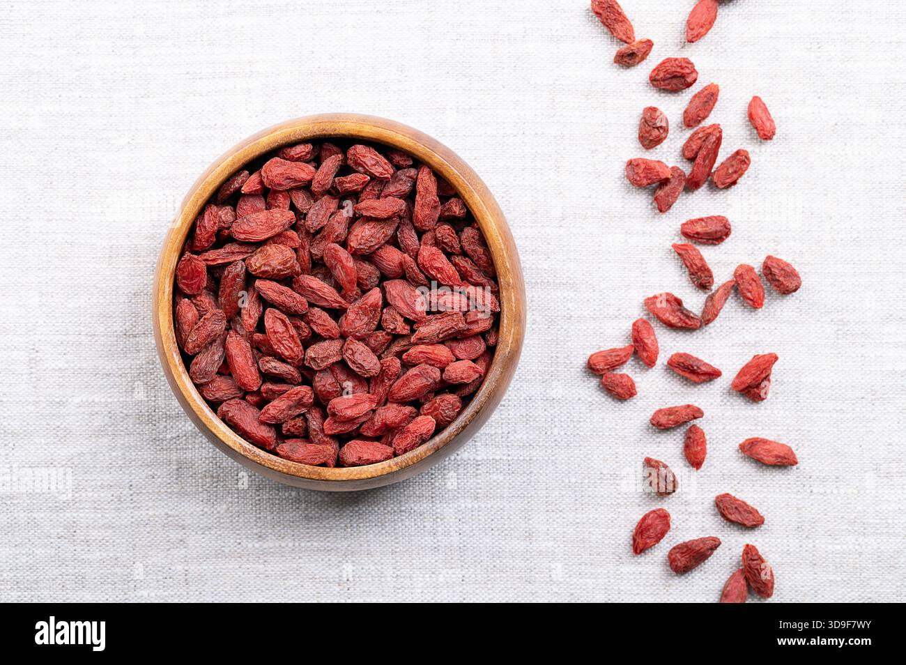 Getrocknete Goji-Beeren, in einer Holzschale auf Leinen. Auch bekannt als chinesische Wolfsbeere, rotes Medlar und Ehebrübe. Leuchtend orange-rote süße Früchte. Stockfoto