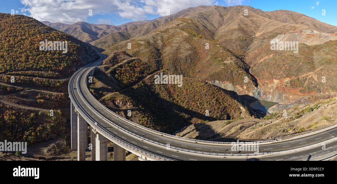 Erhöhter Drohnenblick auf das Autobahnviadukt A1 durch das steile, zerklüftete Gelände von Kolsh im Kreis Kukës, umgeben von herbstlichen Hügeln und dr Stockfoto