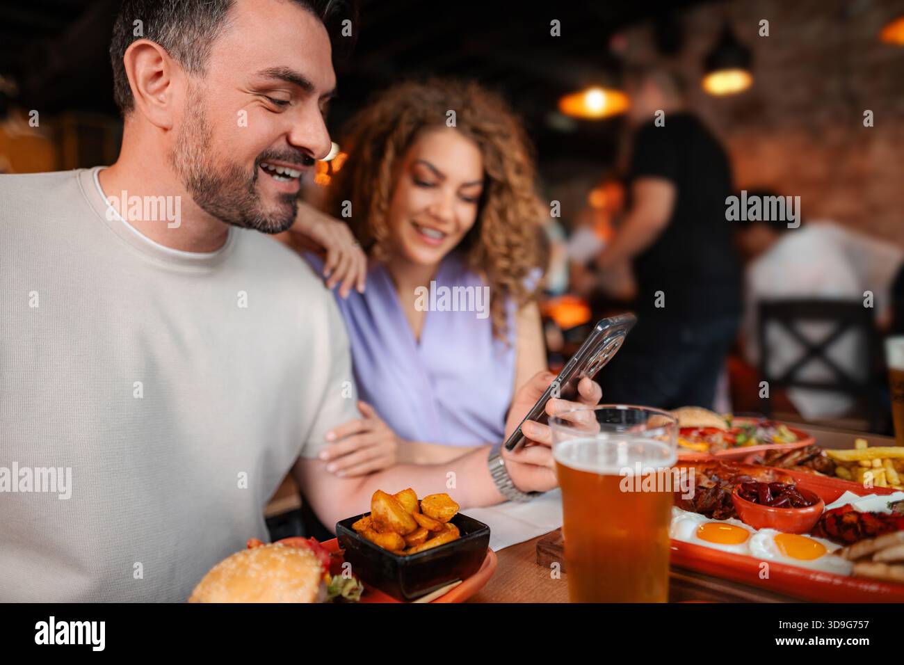 Ein Paar lacht und benutzt das Smartphone beim Mittagessen im Restaurant Stockfoto