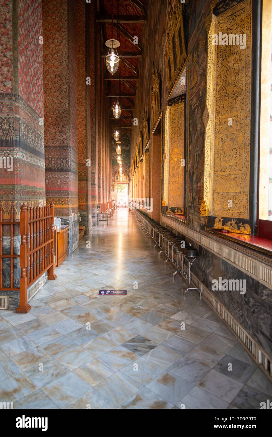 Sonnendurchfluteter Korridor in der Haupthalle des Wat Pho in Bangkok, mit kunstvoll verzierten Wänden und warmem Licht, das durch die Tür strömt, schafft einen Frieden Stockfoto