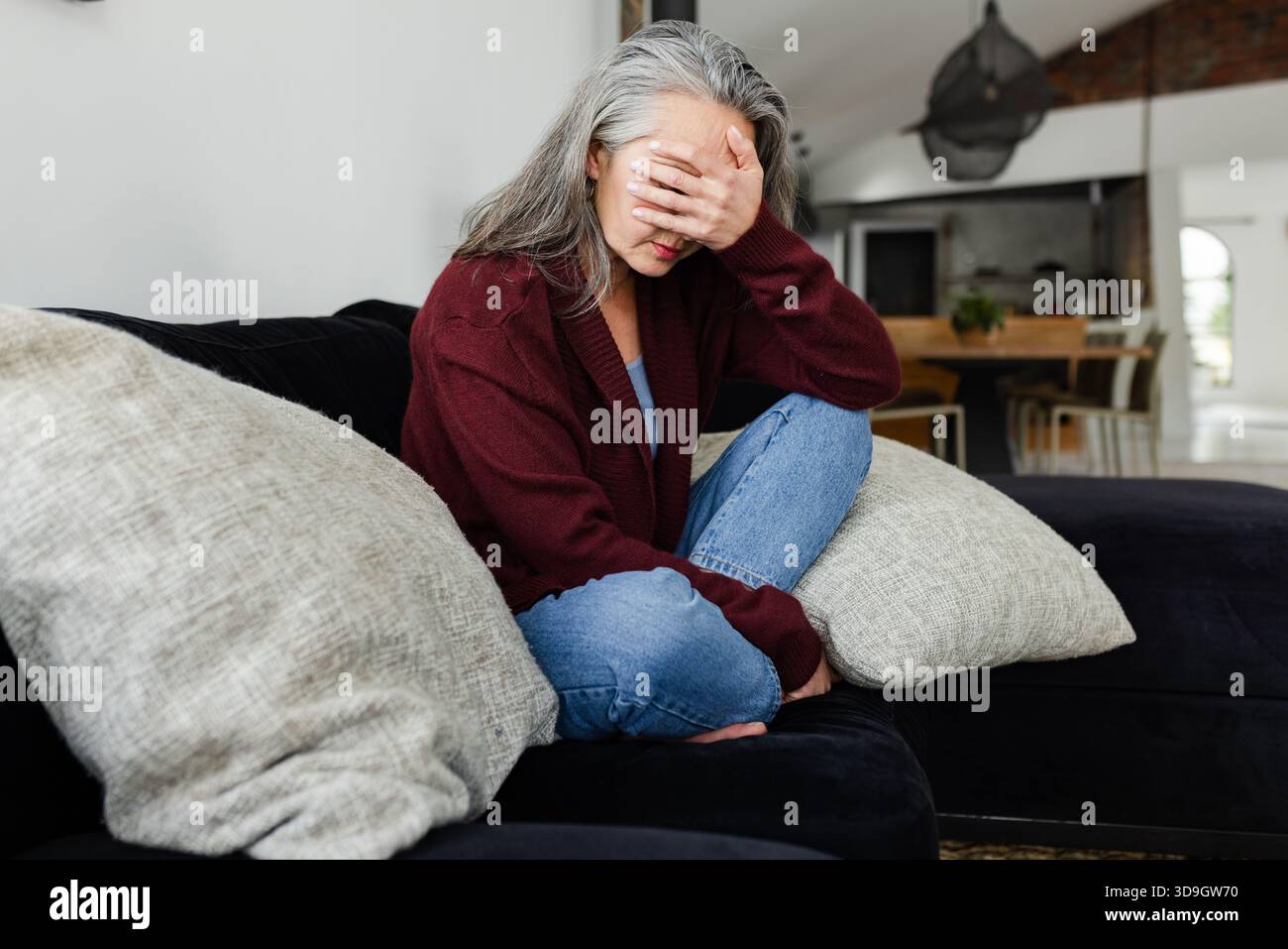 Dunkles Sofa in offenem Wohnbereich mit hellen Kissen, freiliegendem Ziegelstein und Holztisch Stockfoto