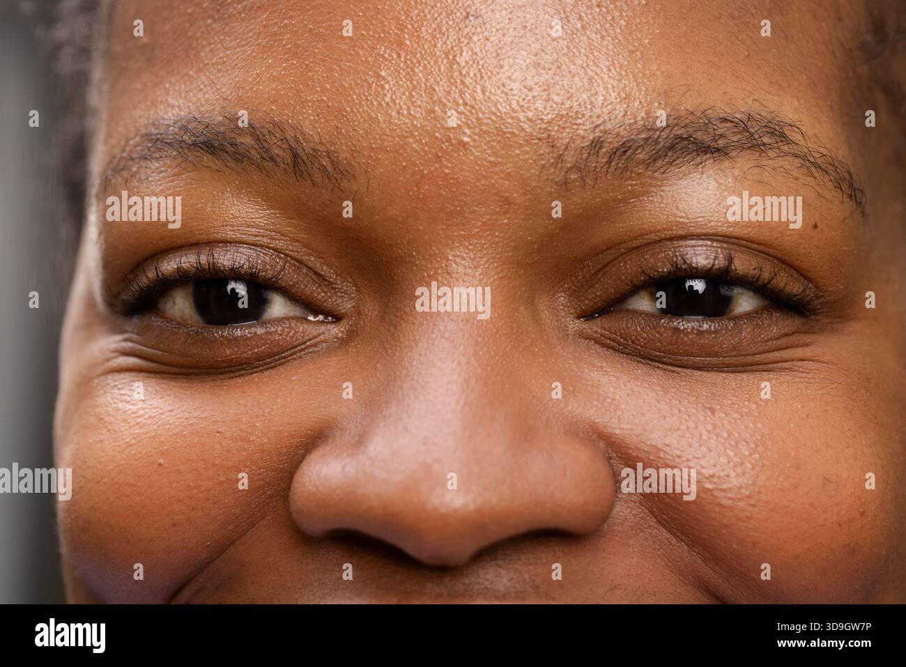 Afroamerikanische Frau zeigt Hautstruktur unter sanfter Beleuchtung im Studio auf grauem Hintergrund Stockfoto