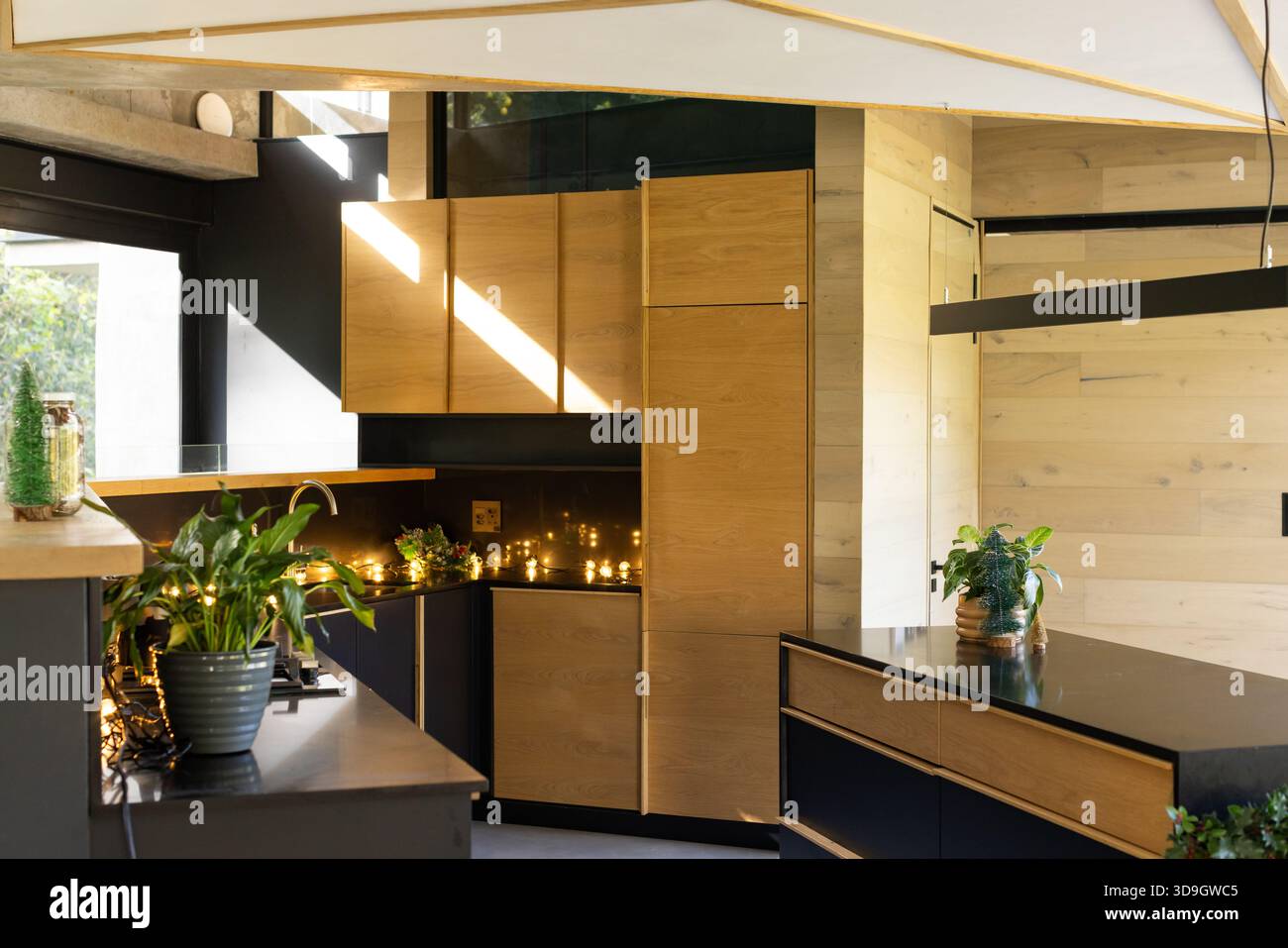 Holzschränke und schwarze Theken zeigen die Kücheninsel mit Feenleuchten und Hängeleuchten unter dem Schrank Stockfoto