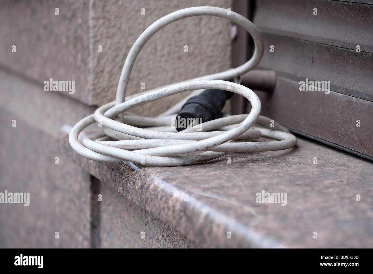 Ein weißes Stromkabel liegt auf einem Steinvorsprung, was auf das städtische Leben hindeutet. Stockfoto