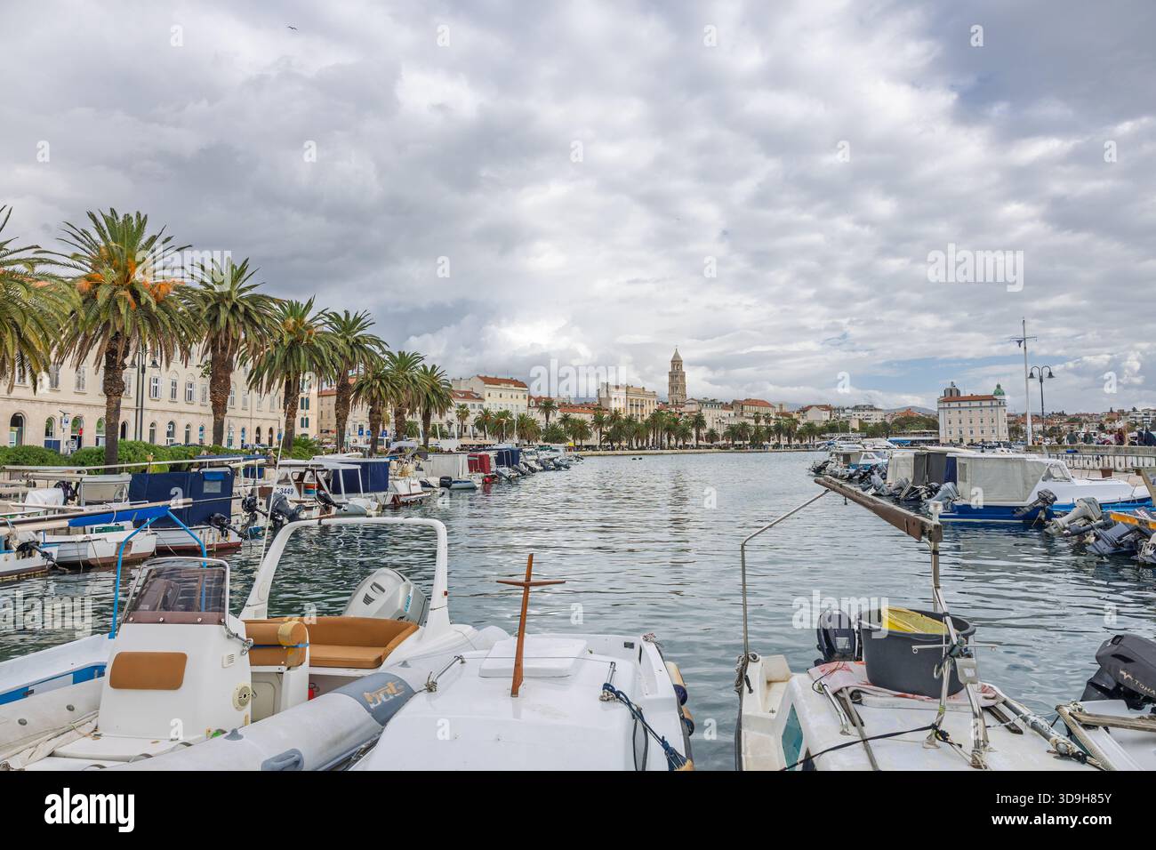 SPLIT, KROATIEN, 10.25.2025: Ein malerischer Hafen gesäumt von Palmen und Booten, umgeben von Steinpromenaden und historischen Gebäuden. Das ruhige Wasser und die Wolke Stockfoto