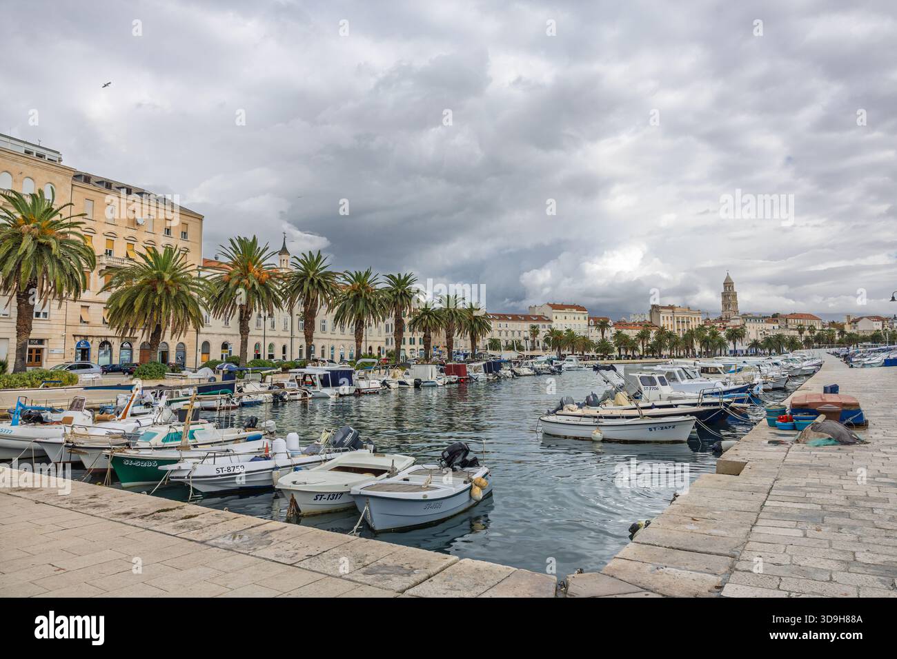 SPLIT, KROATIEN, 10.25.2025: Ein malerischer Hafen gesäumt von Palmen und Booten, umgeben von Steinpromenaden und historischen Gebäuden. Das ruhige Wasser und die Wolke Stockfoto