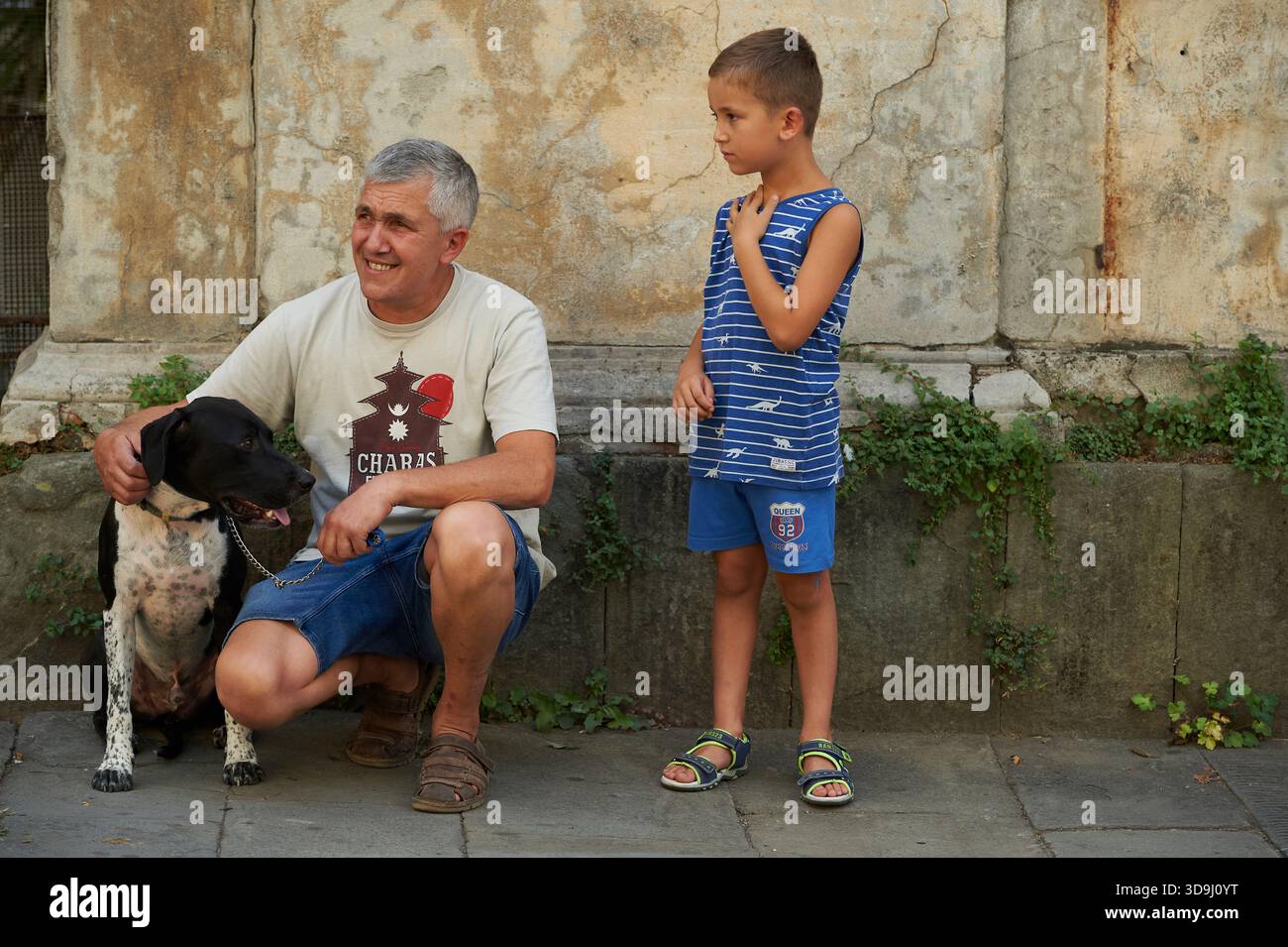 Vater und Sohn mit ihrem Hund auf der Straße in Pescia, Italien, interagieren, während eine Parade vorbei geht. Stockfoto