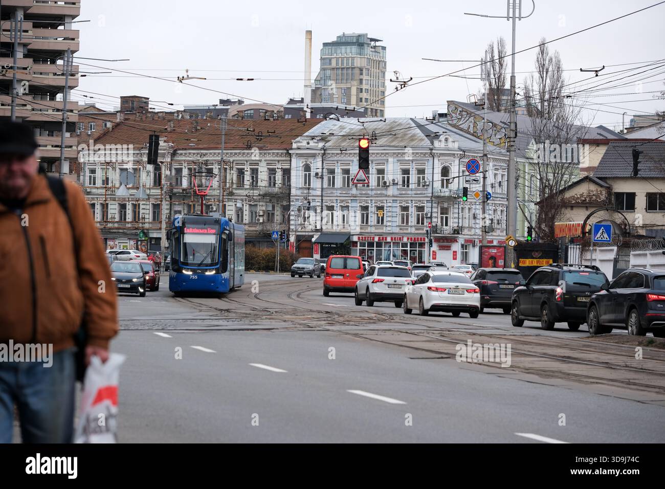 An einer stark frequentierten Kreuzung befinden sich Straßenbahnen und Autos, während Fußgänger auf den Gehwegen herumfahren. Kiew, Ukraine. Dezember 2025. Stockfoto