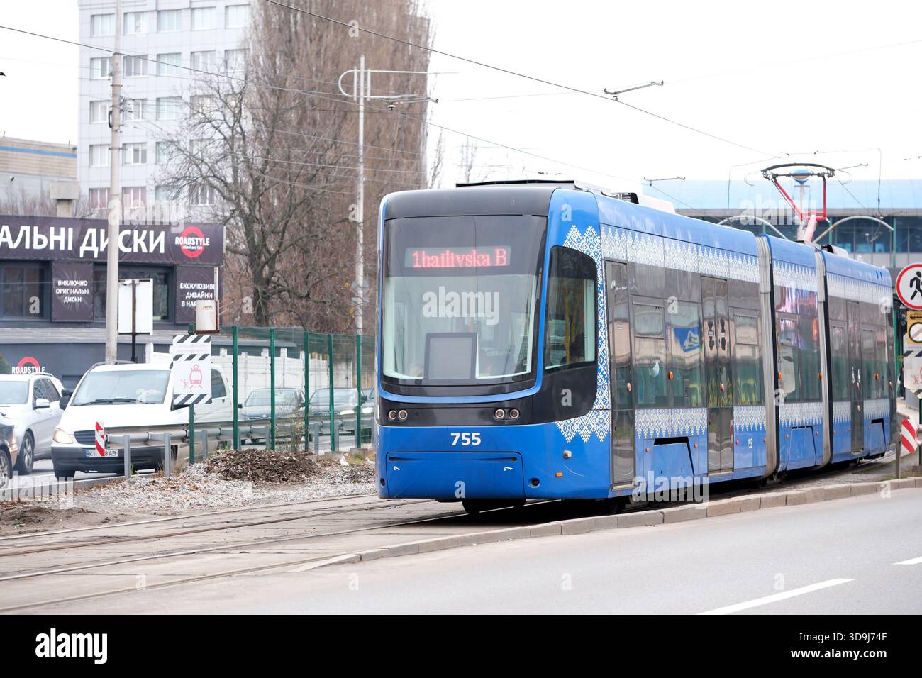 Eine leuchtend blaue Straßenbahn bewegt sich in einem belebten Stadtgebiet stetig auf den Gleisen. Kiew, Ukraine. Dezember 2025. Stockfoto