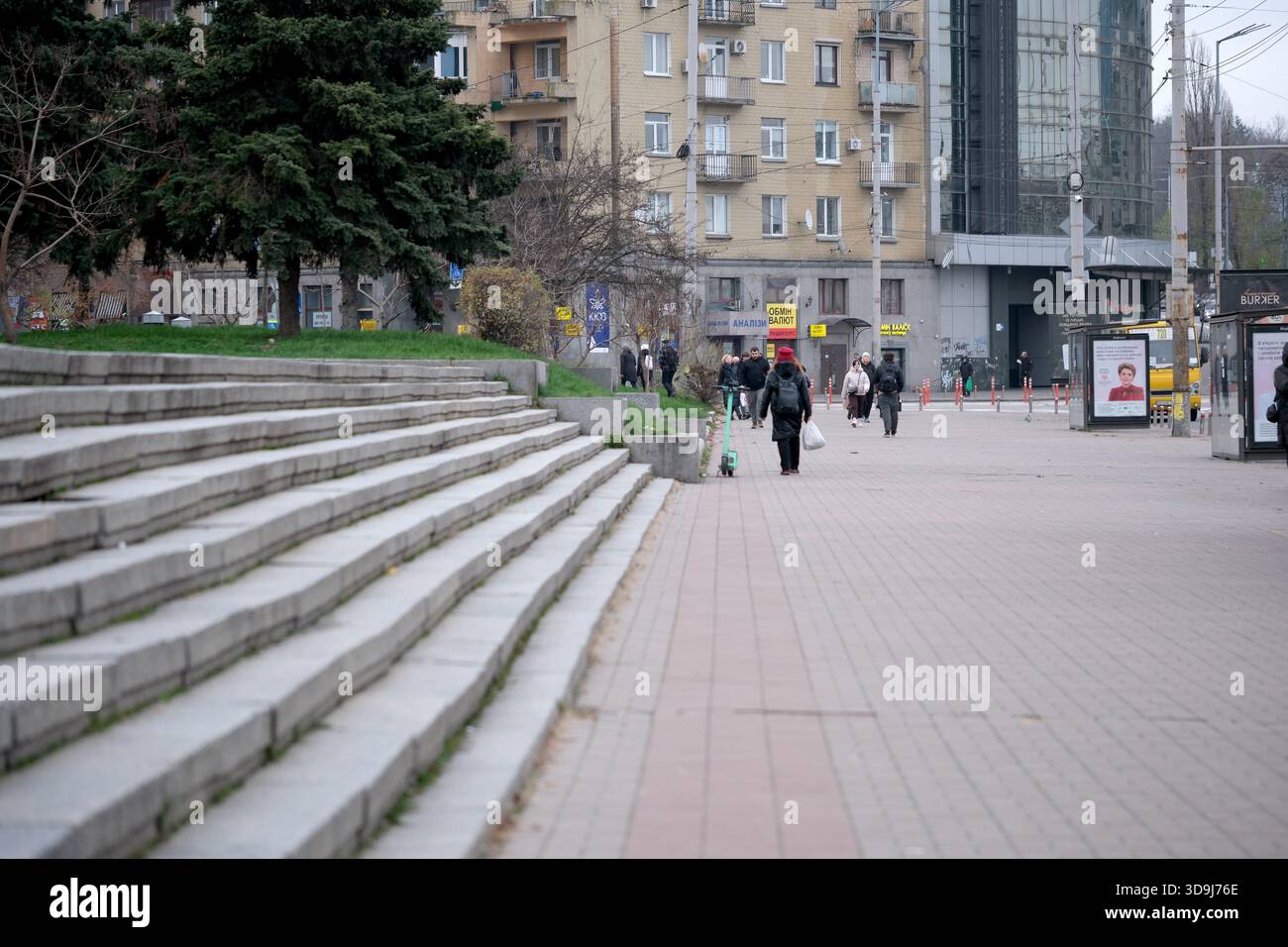 Die Leute schlendern entlang eines Stadtrundgangs, der von Treppen und zeitgenössischer Architektur gesäumt ist. Kiew, Ukraine. Dezember 2025. Stockfoto