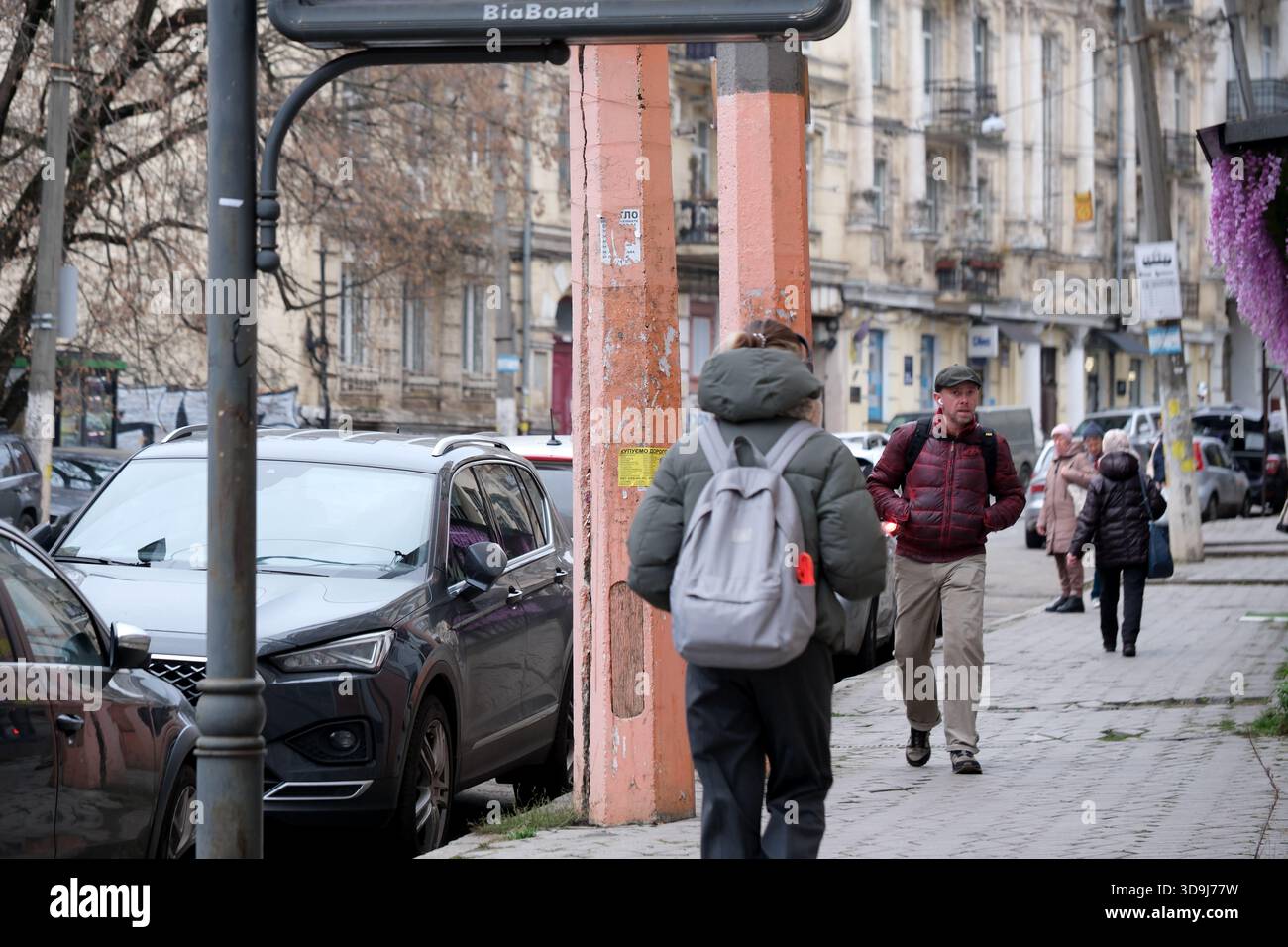 Die Menschen schlendern entlang einer Stadtstraße, während die Fahrzeuge in der Nähe parken, um das tägliche Leben einzufangen. Kiew, Ukraine. Dezember 2025. Stockfoto