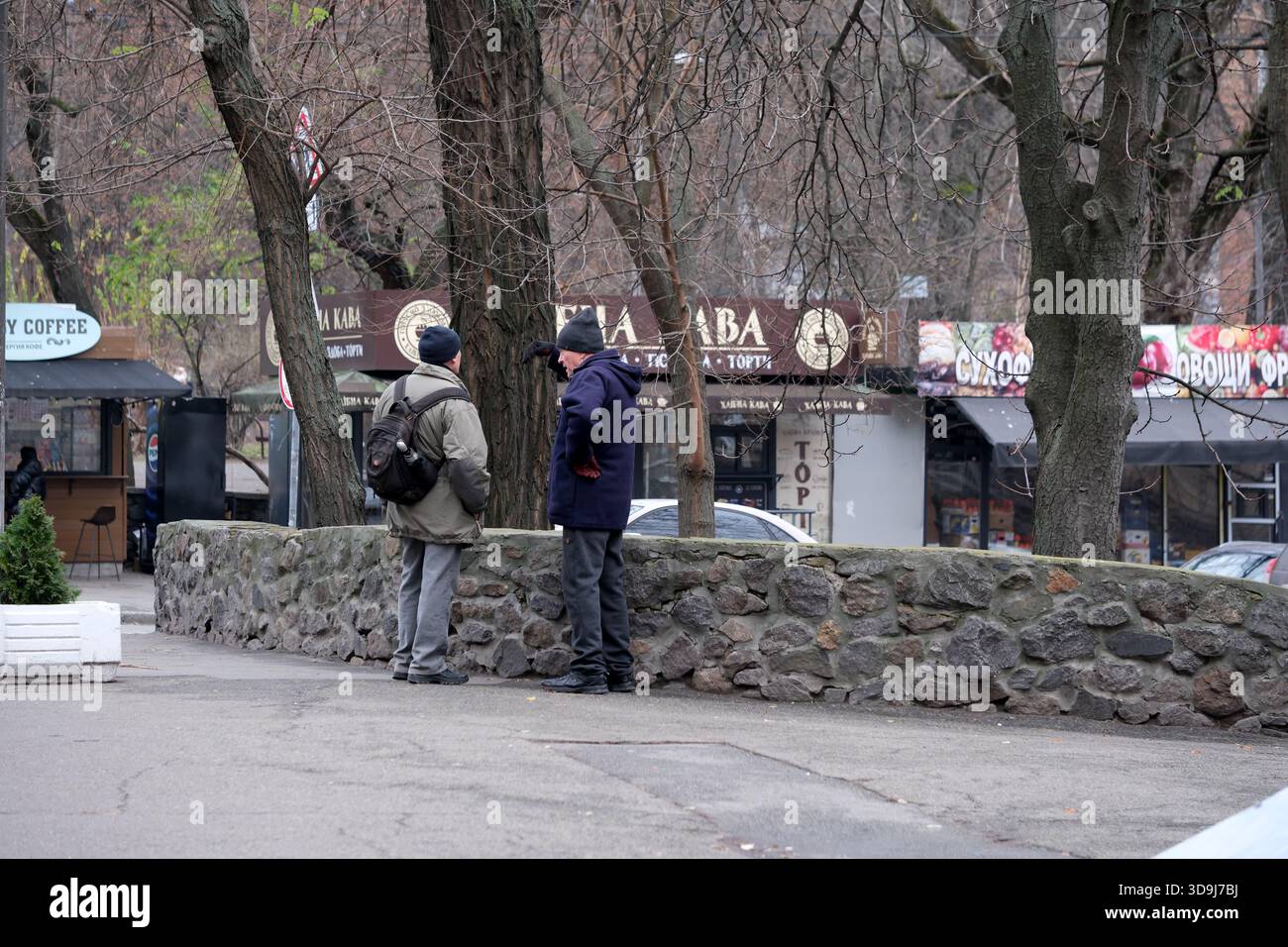 Zwei Männer unterhalten sich und genießen die Gesellschaft des anderen an einer Steinmauer an einem kühlen Nachmittag. Kiew, Ukraine. Dezember 2025. Stockfoto