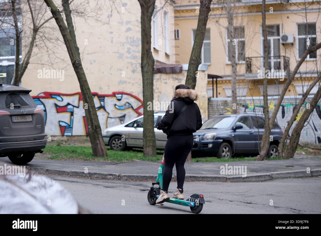 An einem kühlen Tag gleitet eine Person an geparkten Autos vorbei und genießt die Stadtbesichtigung. Kiew, Ukraine. Dezember 2025. Stockfoto